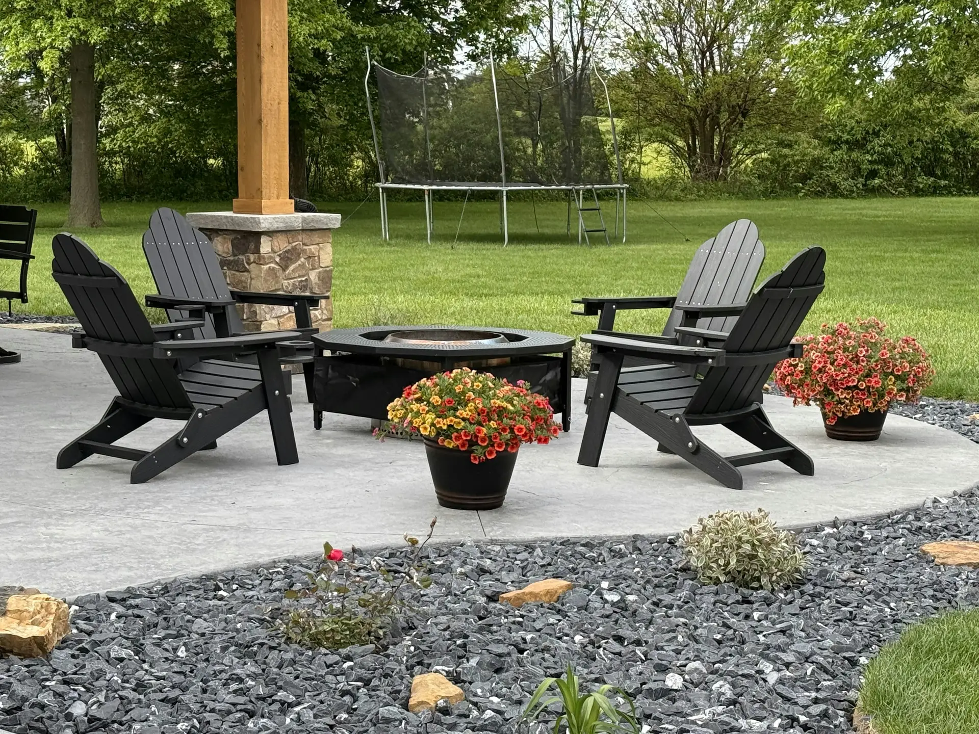 Residential concrete patio with outdoor chairs, a fire feature, and landscaped lawn